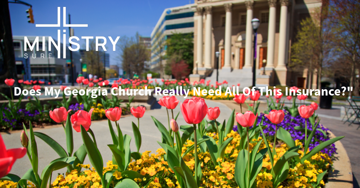 A vibrant image featuring a beautifully landscaped garden with blooming tulips in the foreground. The garden is situated in front of a stately church building. The clear blue sky and springtime setting provide a picturesque backdrop. Overlaid on the image, in bold white text, is the title: "Does My Georgia Church Really Need All Of This Insurance?" The logo of MinistrySure is prominently displayed in the top-left corner.